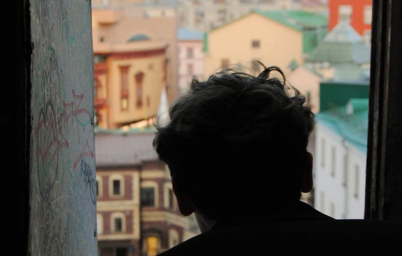 Person looking out a window at a calm city skyline.